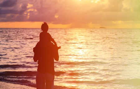 father and daughter looking at sunset on tropical beachの写真素材