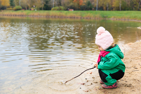 little girl playing with water and stick, kids autumn activitiesの写真素材