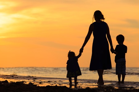 mother and two kids walking on sand beach at sunsetの写真素材