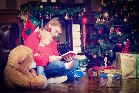 father and little daughter reading book in christmas homeの写真素材