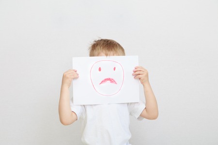 little boy holding sad face mask, depression and sadnessの写真素材
