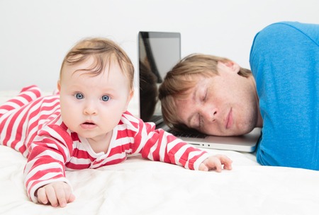 father tired of working from home- parent sleeping on laptop while baby crawlingの写真素材