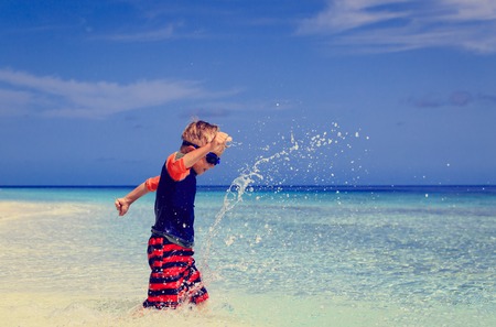 little boy running splashing water on tropical beachの写真素材