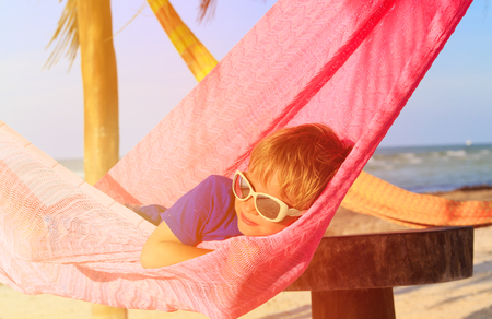 happy little boy relaxed in hammock on sand beachの写真素材