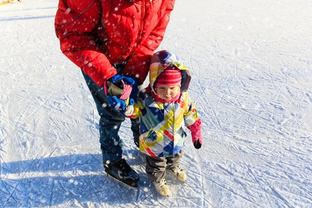 father and child learning to skate in winter snowの写真素材