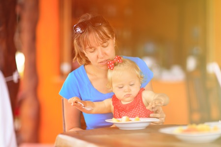 mother feeding cute little daughter in cafeの写真素材