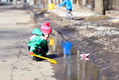 little girl playing with paper boats in spring water puddleの写真素材