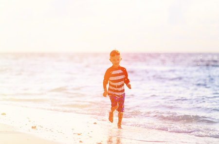 little boy running splashing water on beach at sunsetの写真素材