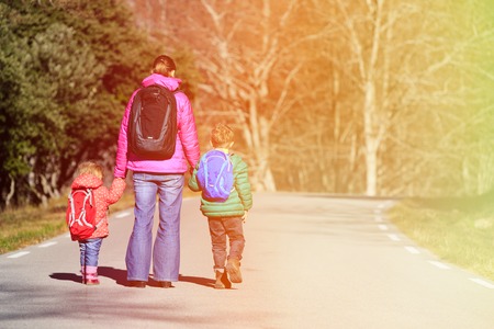 mother and two kids with backpacks walking on the roadの写真素材