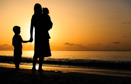mother and two kids walking on sand beach at sunsetの写真素材