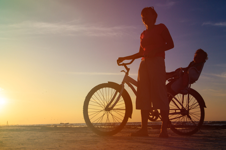 Silhouette of mother and baby biking at sunset beachの写真素材