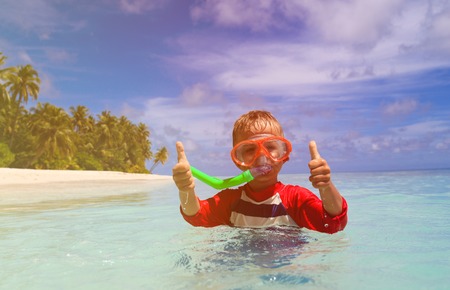 cute happy little boy swimming with thumbs up at beach