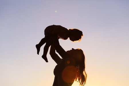 mother and little daughter play at sunset skyの写真素材