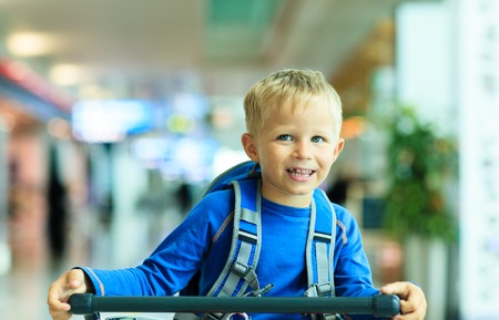 Happy cute little boy at airport riding on luggage cart, kids travelの写真素材