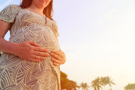 happy pregnant woman on beach touching her belly with loveの写真素材