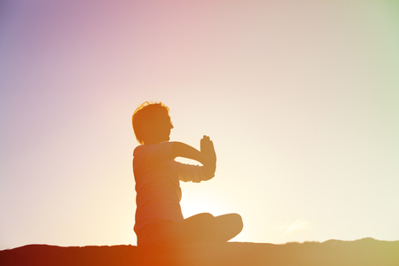 ilhouette of young man doing yoga at sunset beachの写真素材