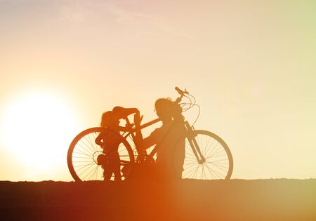 Silhouette of father and little daughter biking at sunset beachの写真素材