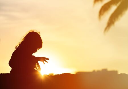 Silhouettes of little girl play at sunset tropical beachの写真素材