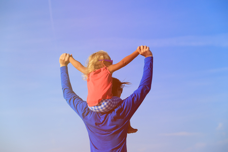 father and little daughter on shoulders play at skyの写真素材