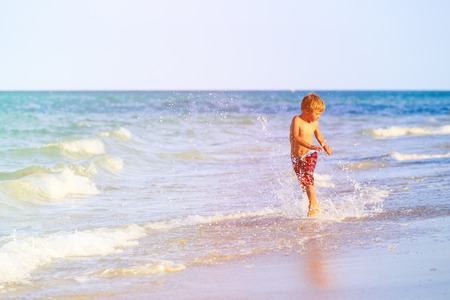 happy little boy running splashing water on beachの写真素材