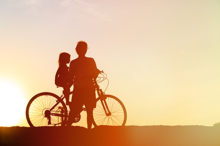 Silhouette of father and little daughter biking at sunset skyの写真素材