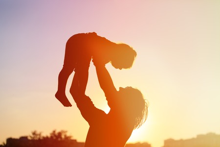 Father and little daughter silhouettes play at sunset skyの写真素材