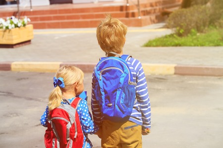 kids go to school- little boy and girl with backpacks near school or daycare buildingの写真素材
