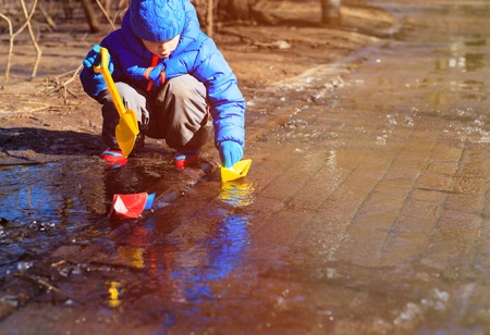 little boy plaing with paper boats in water puddle, kids seasonal activitiesの写真素材