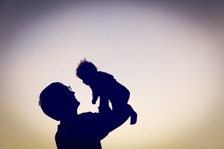 silhouettes of father and little baby playing at sunset skyの写真素材