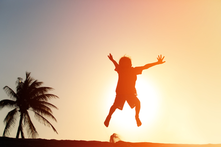happy boy jumping at sunset tropical beachの写真素材