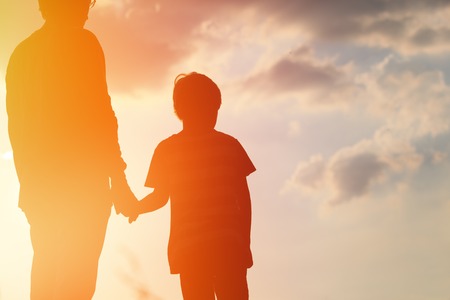 silhouette of father and son holding hands at sunset skyの写真素材
