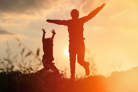happy father and son jumping at sunset skyの写真素材