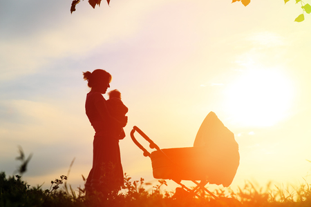 Silhouette of mother with little baby at sunset, happy familyの写真素材