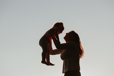 mother and little daughter play at sunset skyの写真素材