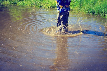 little boy in rain boots jumping into water puddle, kids seasonal activities