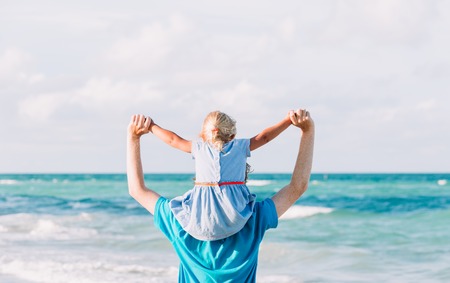 father and daughter on shoulders play at sky on beachの写真素材