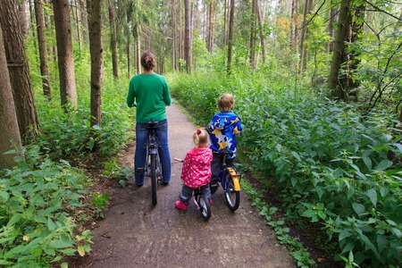 mother with little son and daughter riding bikes in summer forestの写真素材