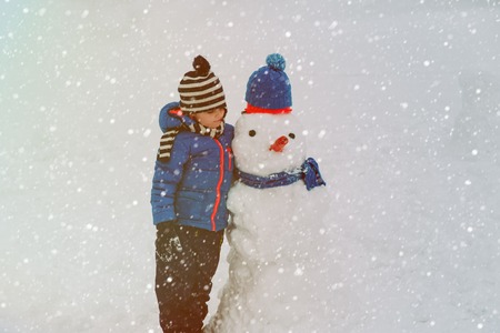 little boy playing with snowman in winter natureの写真素材