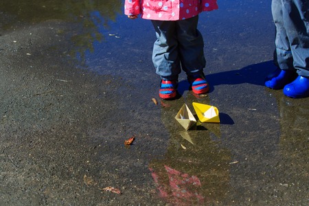 little boy and girl playing with paper boats in water puddleの写真素材