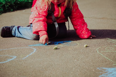 little girl drawing with chalks on asphalt after schoolの写真素材