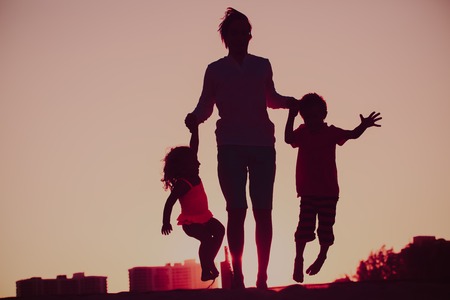 happy family - father with son and daughter jumping from joy in sunset natureの写真素材