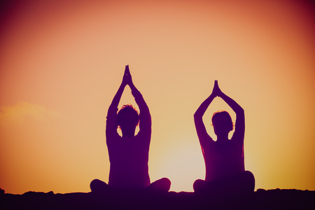 silhouette of couple doing yoga at sunset skyの写真素材