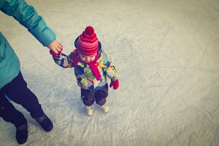 mother teaching little daughter to skate in winter snowの写真素材
