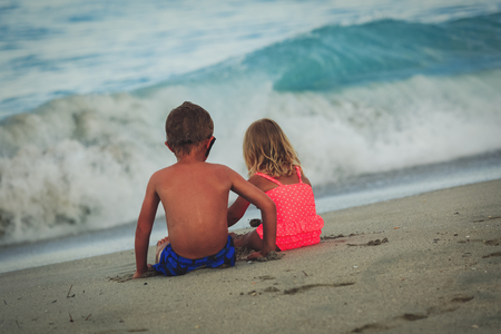 friendship and family at beach- little boy and girl looking at sea wavesの写真素材