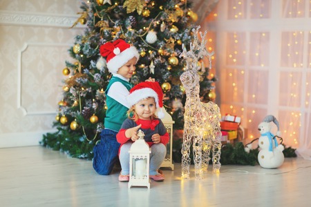 cute little boy and girl waiting for presents in decorated living roomの写真素材