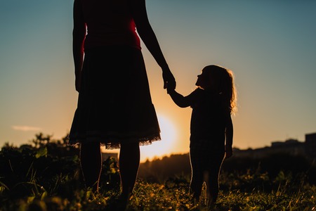silhouette of mother and daughter holding hands in sunset natureの写真素材