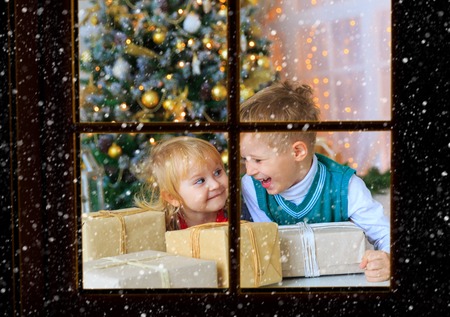 Kids opening christmas presents in decorated living room viewed through window from outside, Christmas celebrationの写真素材