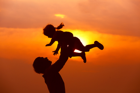 Father and little daughter silhouettes play at sunset skyの写真素材