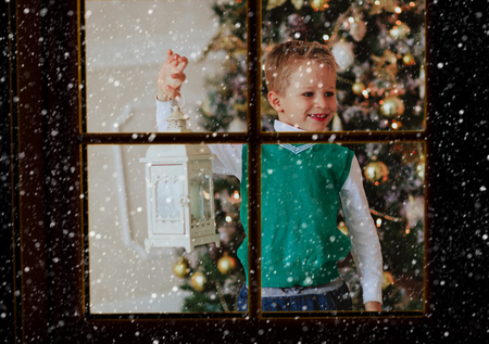 little boy holding Christmas lantern in decorated living room viewed from outside windowの写真素材