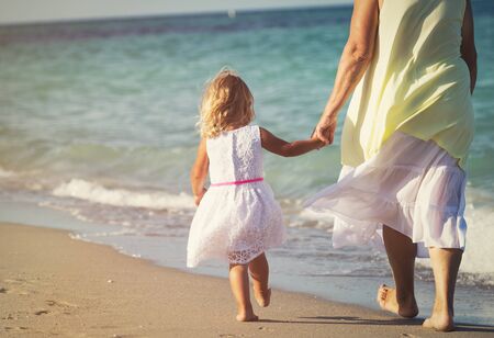 Happy grandmother with little girl walk at beach, active retirementの写真素材